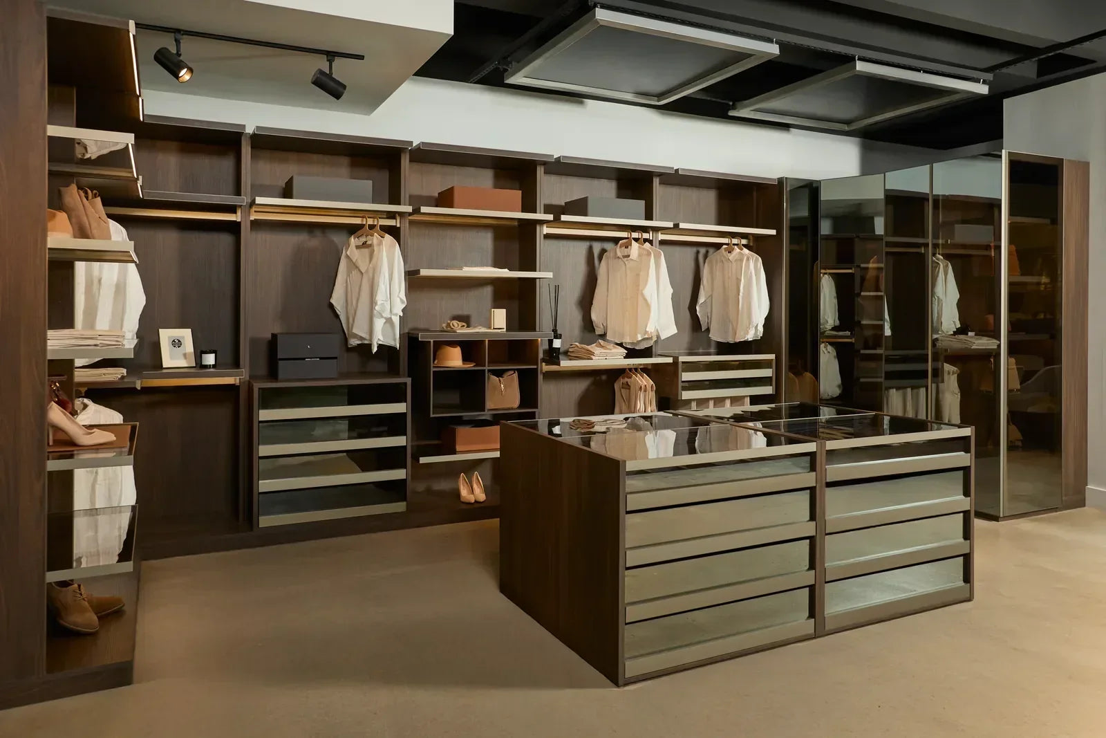 Spazio2 large walk-in closet with wall-to-wall dark wood cabinetry, open shelving, hanging rods, and drawer units spanning the full room width, centered around a large mirrored double island