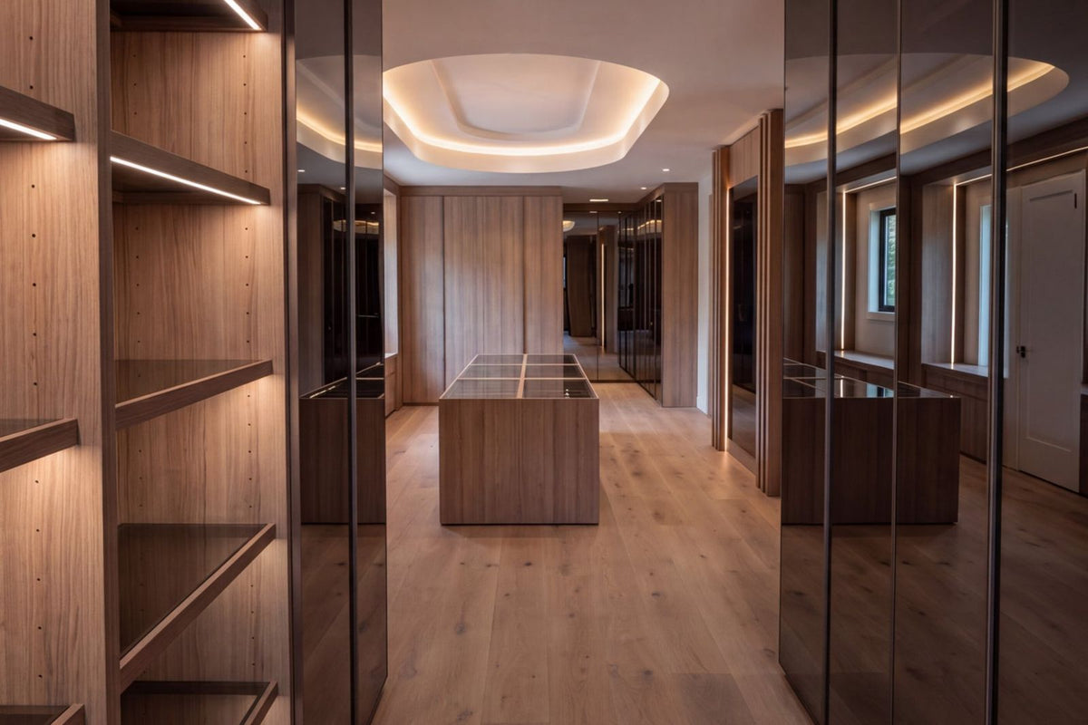 An empty LAZZONI dressing room in warm oak, showing the shelving structure, a glass-topped island and concealed cove lighting before anything has been put away