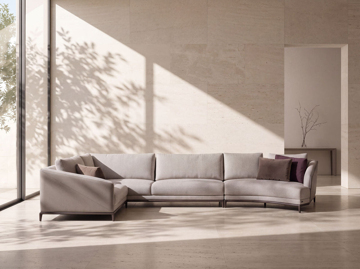A pale woven modular sofa turned into an L against a travertine wall, dappled daylight across it, the separate seat units and the corner module legible