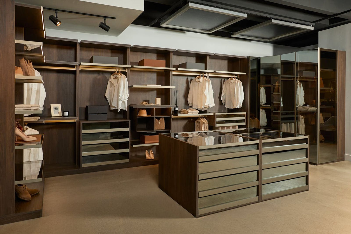 A LAZZONI walk-in closet in dark walnut, with open shelving and double-hung rails along the wall, track lighting overhead and a pair of glass-topped drawer islands at the center