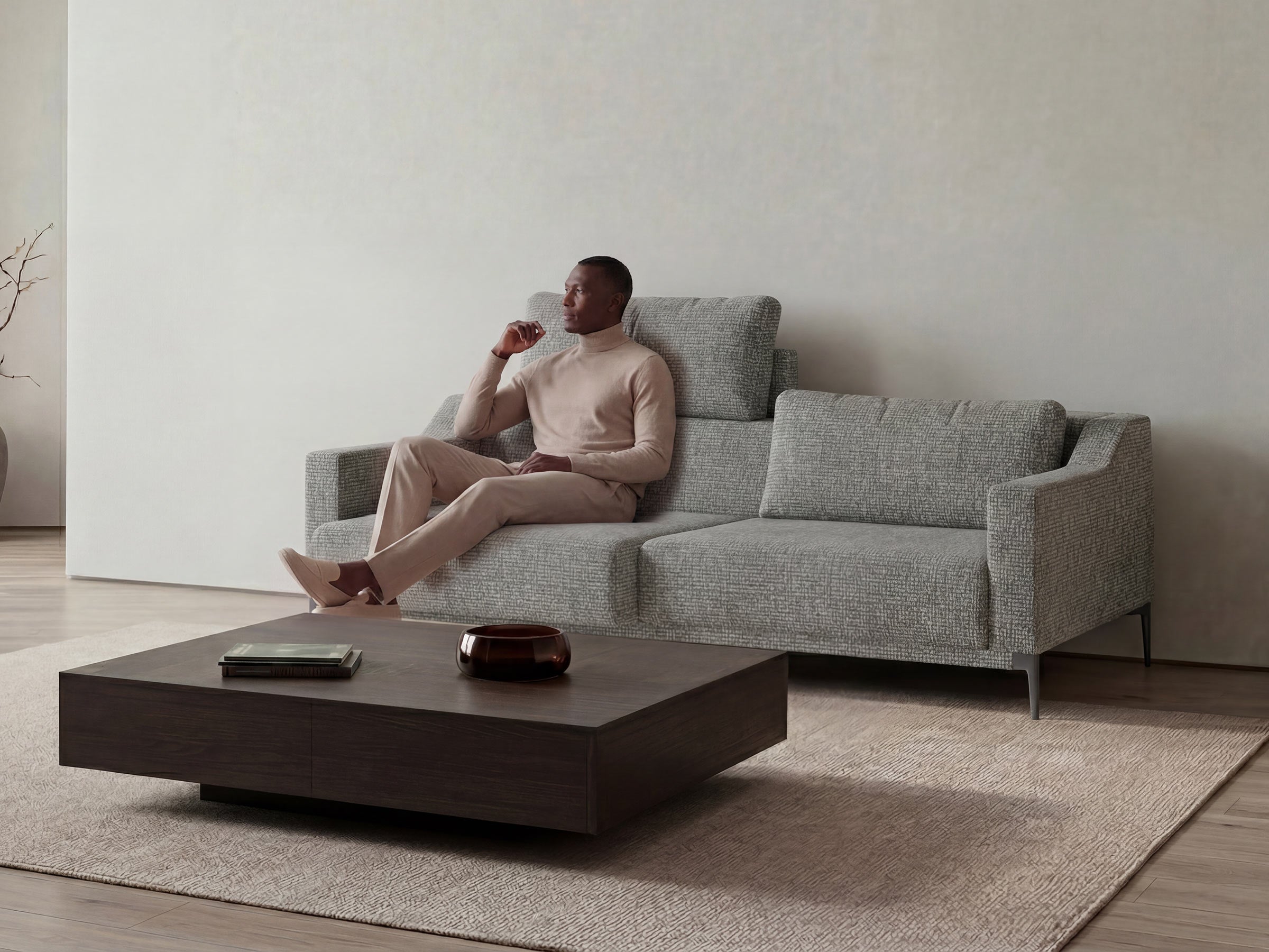 Man sitting on a gray sofa in a minimalistic living room with a wooden coffee table.
