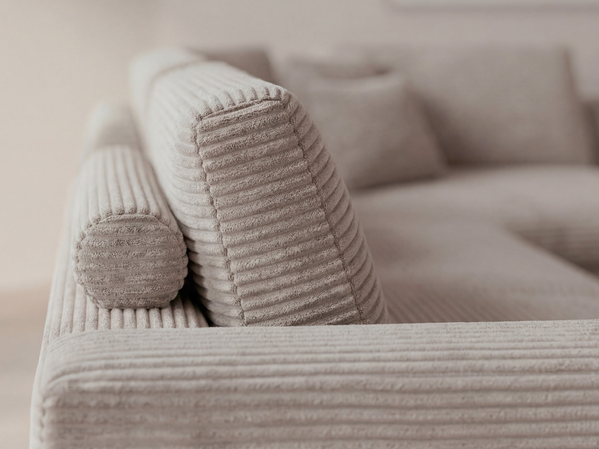 Beige corduroy sofa with decorative cushions on a neutral background