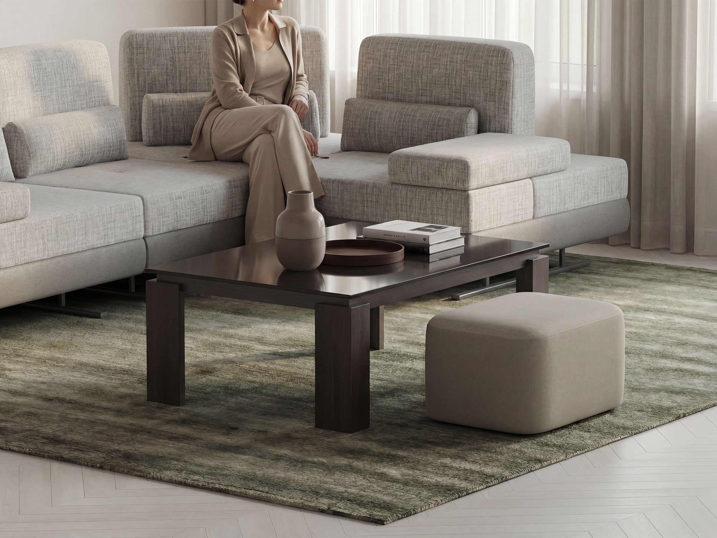 Woman sitting on a modern gray sofa in a living room with a coffee table and ottoman.