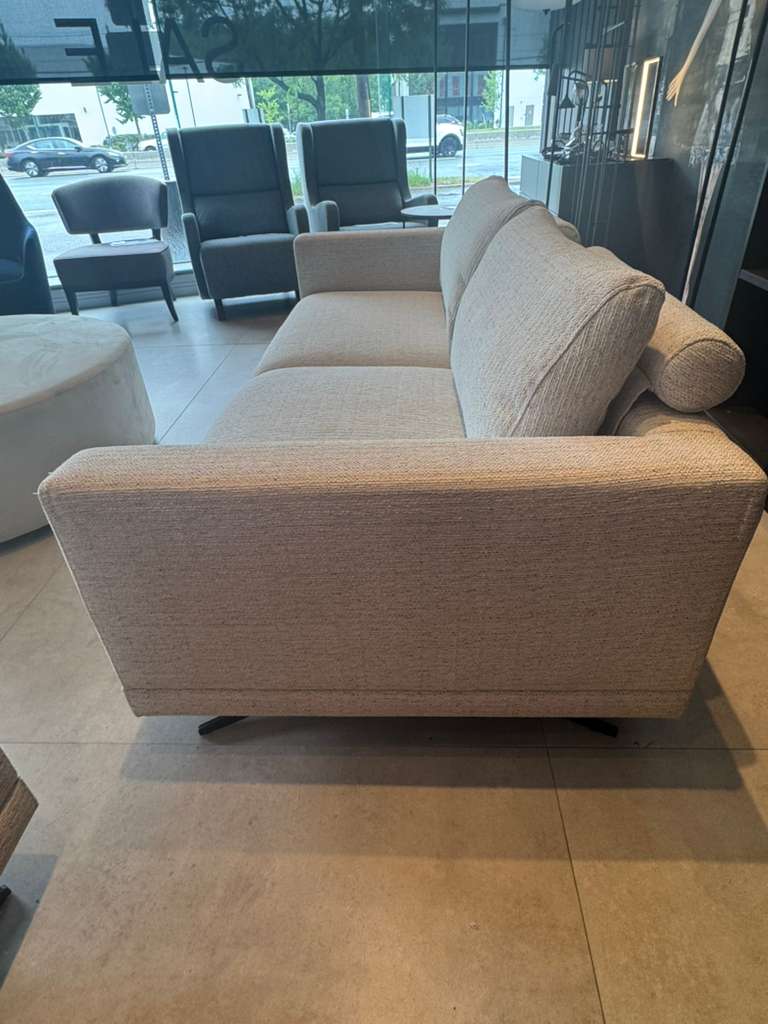 Beige sofa in a showroom setting with reflective floor and glass walls.