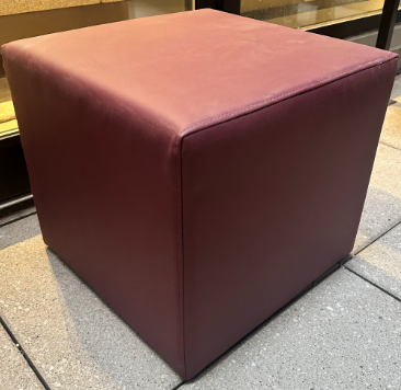 Cube-shaped ottoman with a maroon fabric cover on a concrete floor.