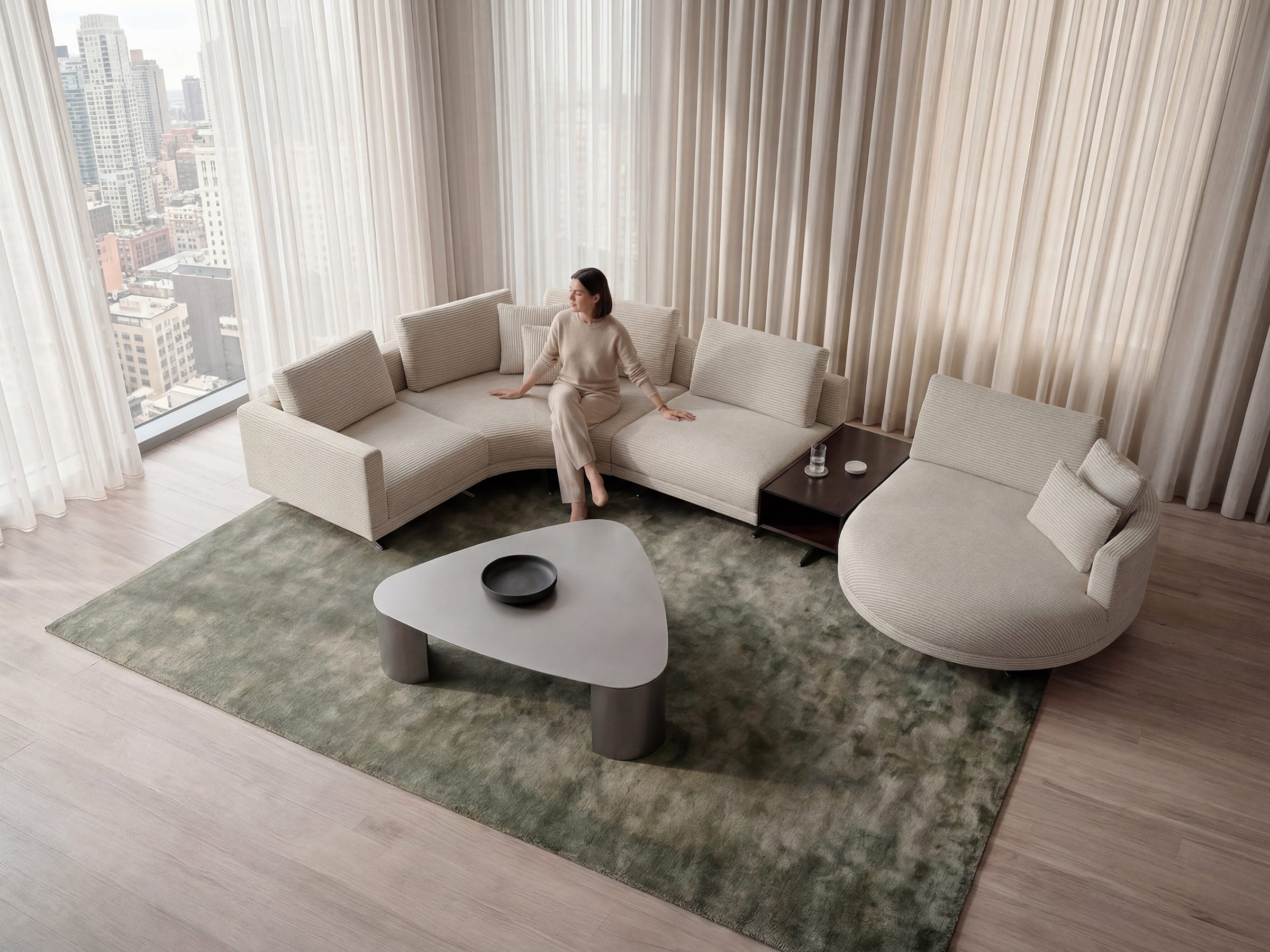 Modern living room with a woman sitting on a sectional sofa, large windows, and a green rug.